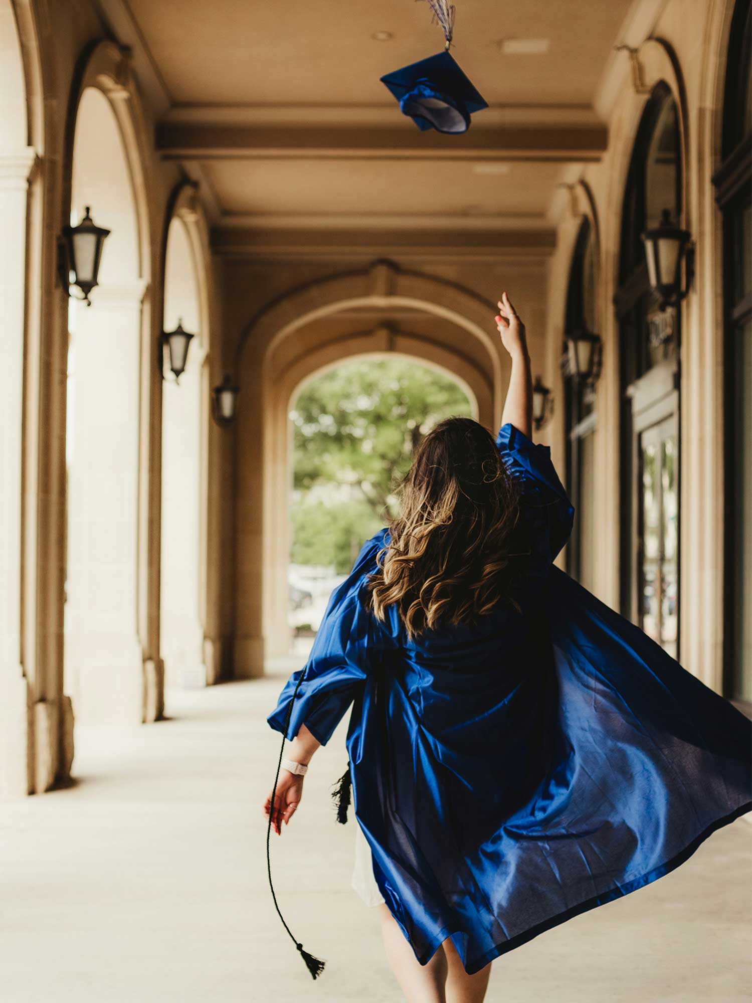 Female graduate in blue cap and gown throwing her cap into the air