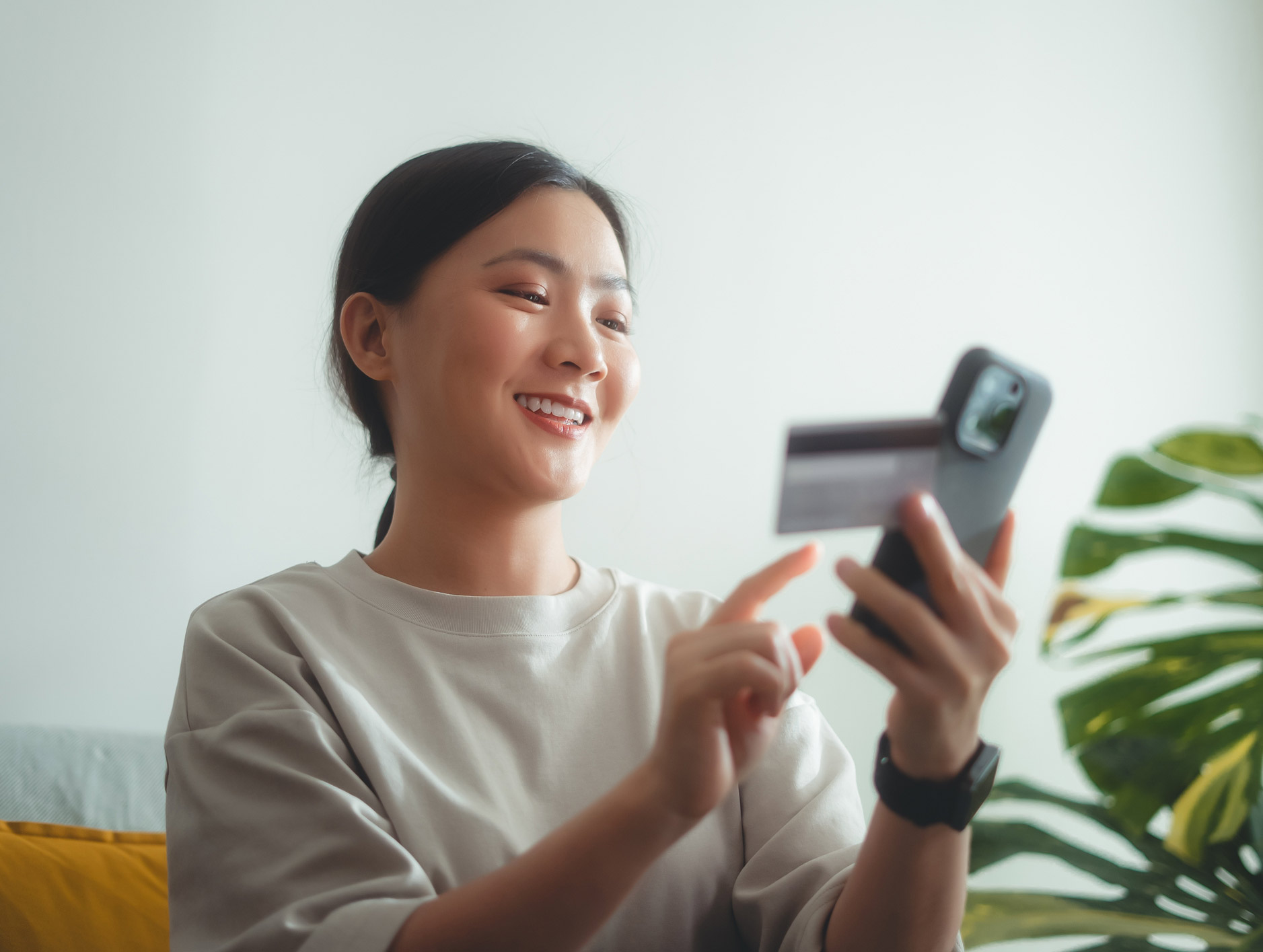 Woman sitting on her sofa smiling at her credit card balance on her smart phone.