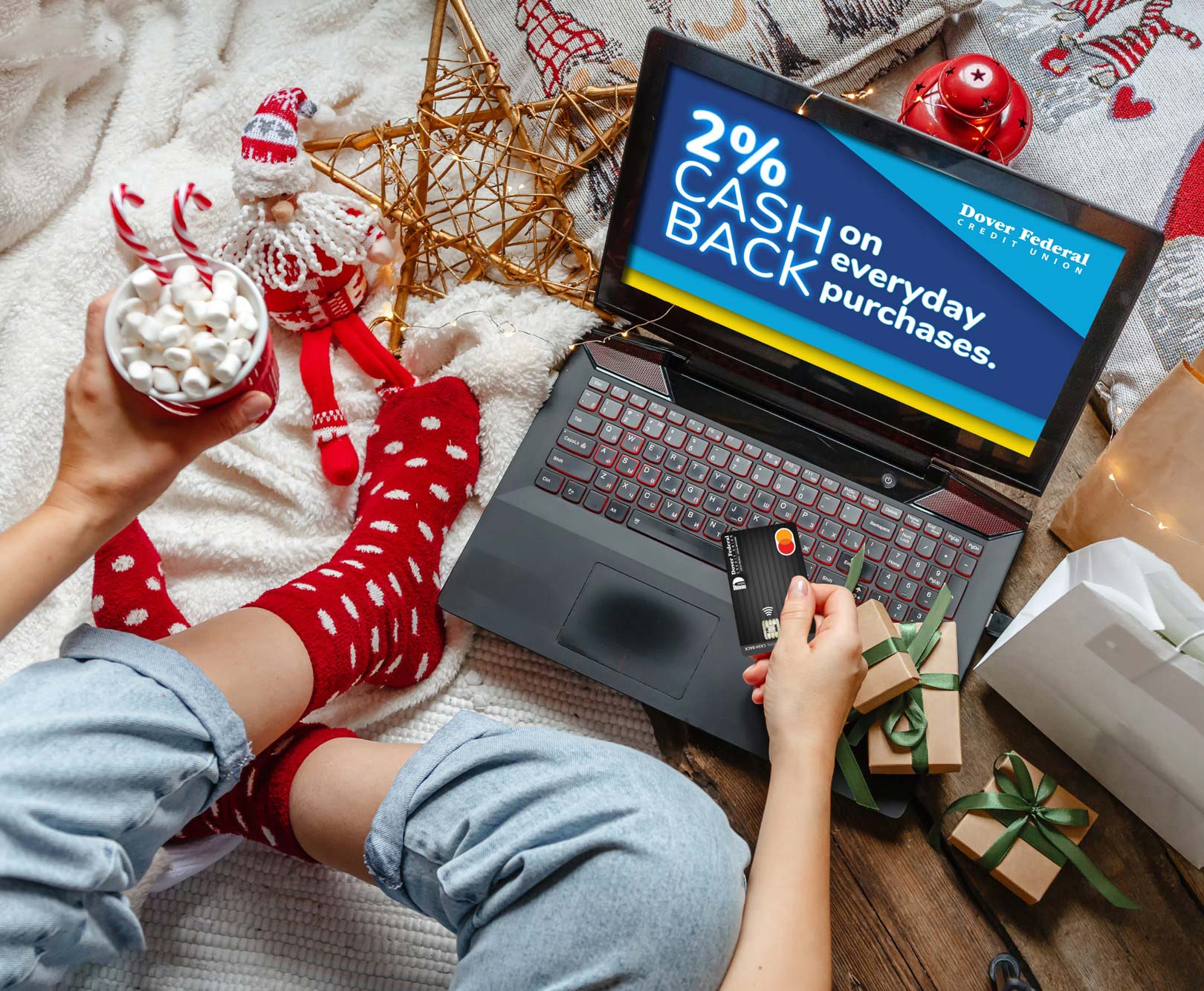 A person drinking hot chocolate with marshmallows in a holiday setting using their laptop to consolidate debt with a Dover Federal Credit Union Mastercard.