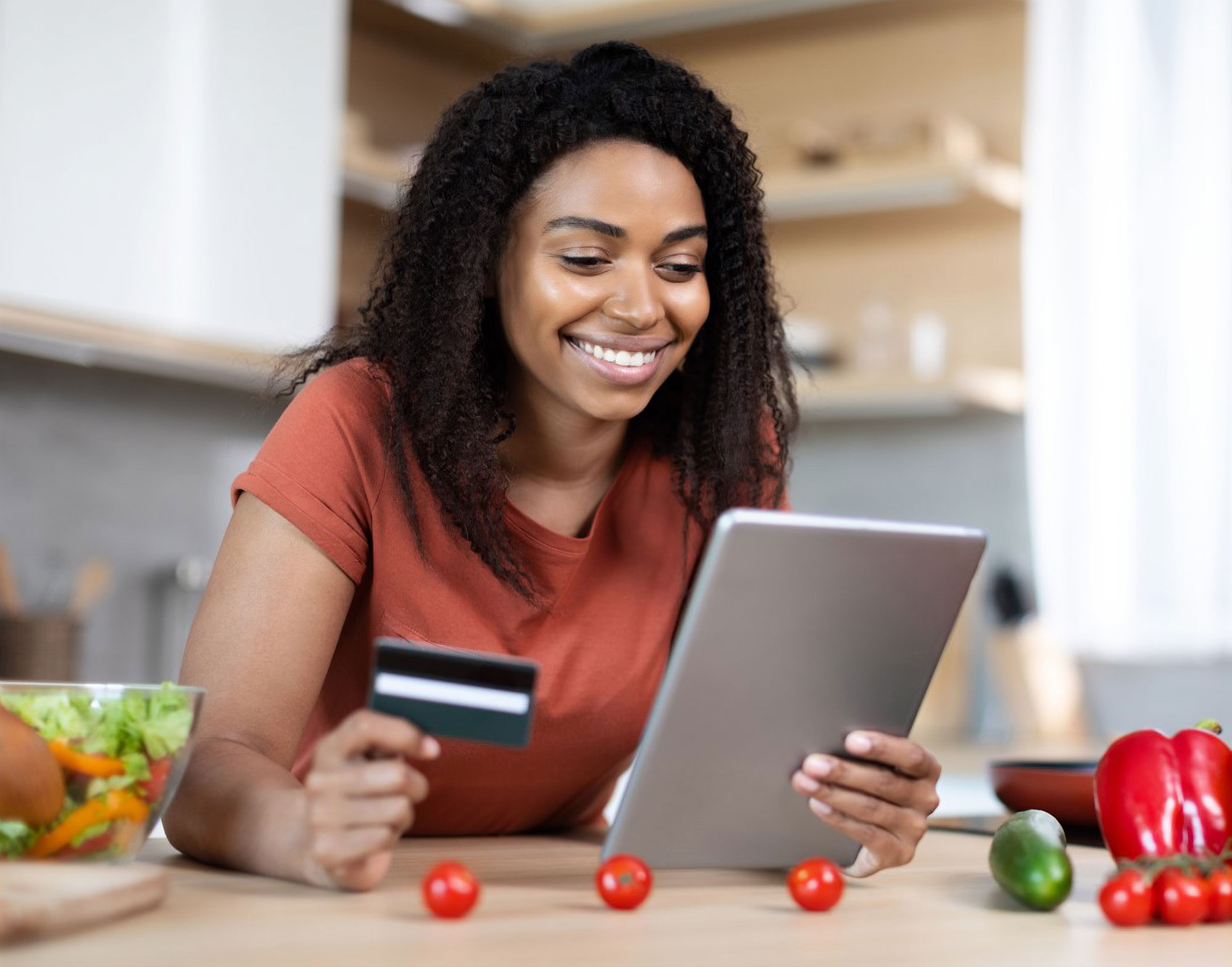 Woman smiling with smartphone and credit card in the kitchen making a salad.