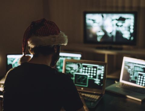 Man sitting in the dark in a Santa Hat with multiple screens in front of him.